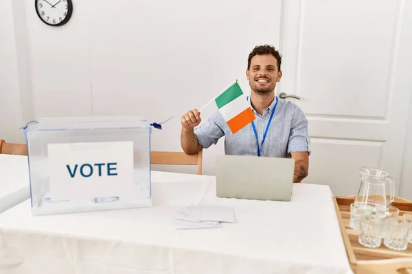 Joven Hispano Sonriendo Confiado Sosteniendo Bandera Irlanda Trabajando Colegio Electoral —  Fotos de Stock