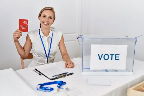 Young blonde woman at political campaign election holding swiss passport looking positive and happy standing and smiling with a confident smile showing teeth