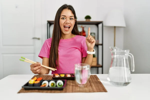 年轻的黑发女人在吃寿司时 用筷子指着手指 提出了一个成功的主意 又兴奋又快乐第一大 — 图库照片