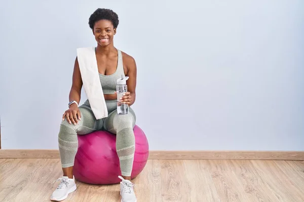African american woman wearing sportswear sitting on pilates ball with a happy and cool smile on face. lucky person.