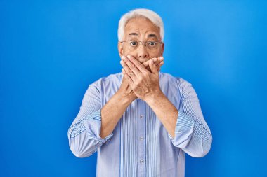 Hispanic senior man wearing glasses shocked covering mouth with hands for mistake. secret concept. 