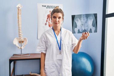Young woman holding pelvis radiography thinking attitude and sober expression looking self confident 