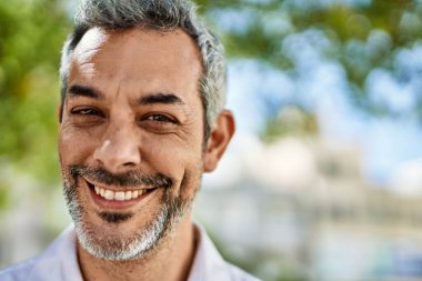 Orta yaşlı, kır saçlı, gülümseyen bir adam şehirde mutlu bir şekilde duruyor..