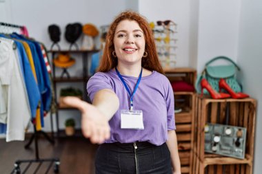 Perakende mağazasında yönetici olarak çalışan genç kızıl saçlı kadın selamlaşma ve hoş geldin demek için gülümseyerek tokalaşıyor. başarılı iş. 