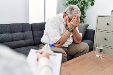 Orta yaşlı, kır saçlı bir adam psikoloji kliniğinde elleriyle psikoloji seansı yapıyor.