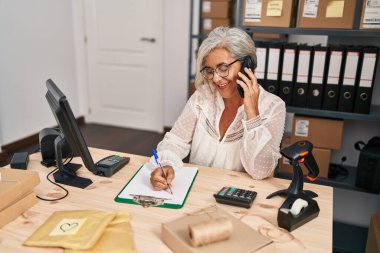 Orta yaşlı kadın ecommerce iş işçisi akıllı telefondan konuşuyor ofisteki panoya yazı yazıyor.