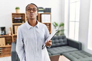 African woman working at psychology clinic looking at the camera blowing a kiss on air being lovely and sexy. love expression. 