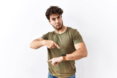 Hispanic man standing over isolated white background in hurry pointing to watch time, impatience, upset and angry for deadline delay 