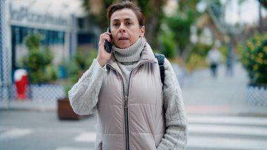 Orta yaşlı İspanyol kadın caddede akıllı telefondan konuşuyor.