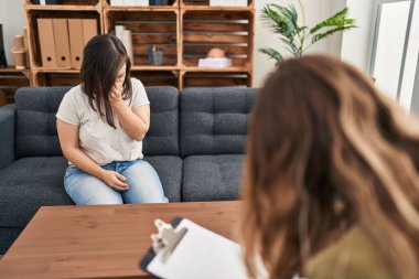 Hispanic girl with down syndrome doing therapy tired rubbing nose and eyes feeling fatigue and headache. stress and frustration concept. 