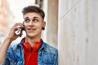 Duvara yaslanmış akıllı telefon kullanarak gülümseyen beyaz bir genç.