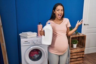 Çamaşır deterjanı şişesini tutan genç hamile kadın zaferi mutlu bir gülümsemeyle ve kazanan yüz ifadesiyle kutluyor. 