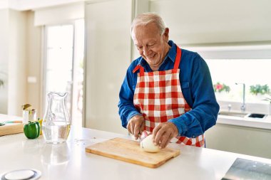 Son sınıf öğrencisi gülümsüyor. Mutfakta soğan doğruyor.