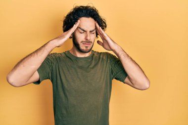 Yakışıklı, yeşil tişörtlü, elleri başının üstünde, stresten dolayı başı ağrıyan bir İspanyol. migren ağrısı. 