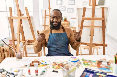Sanat stüdyosundaki Afrikalı Amerikalı sanatçı el hareketleriyle olumlu jest yapıyor, gülümsüyor ve mutlu. Neşeli ifade ve kazanan jest. 