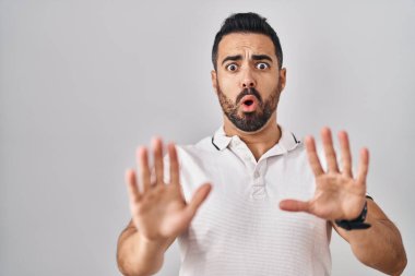 Young hispanic man with beard wearing casual clothes over white background moving away hands palms showing refusal and denial with afraid and disgusting expression. stop and forbidden. 
