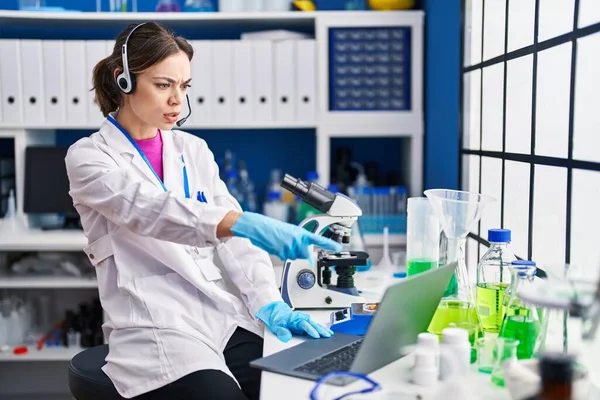 Hispanic woman working at scientist laboratory pointing with finger to the camera and to you, confident gesture looking serious