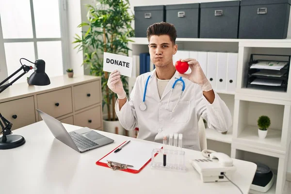 Young Hispanic Doctor Man Supporting Organs Donations Puffing Cheeks Funny — Stock Fotó