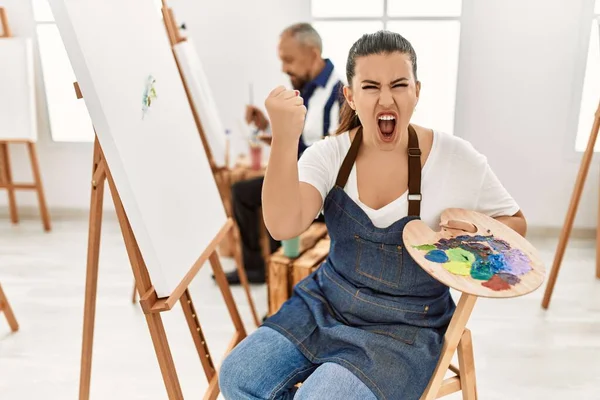 Young artist woman at art studio annoyed and frustrated shouting with anger, yelling crazy with anger and hand raised