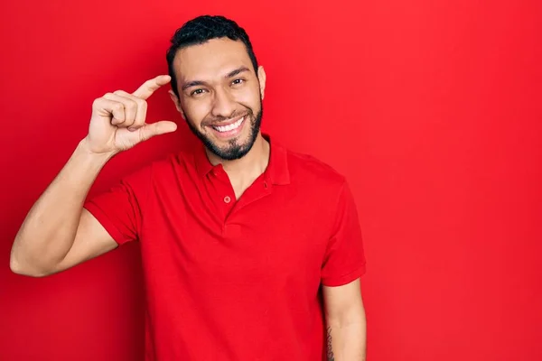 髭を生やしたヒスパニック系の男性は カジュアルな赤いTシャツを着て笑顔と指を見て カメラで小さなサイズの看板を行う手で自信を持ってジェスチャー 概念を測定し — ストック写真