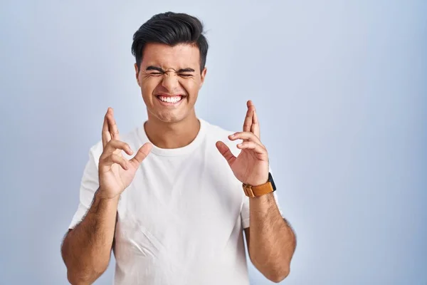 Uomo Ispanico Piedi Sopra Sfondo Blu Gesticolando Dito Incrociato Sorridente — Foto Stock