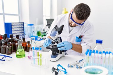 Laboratuvarda mikroskop kullanarak bilim adamı üniforması giyen genç bir İspanyol.