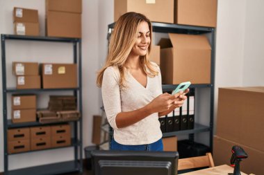 Ofiste akıllı telefon kullanan genç sarışın bir iş kadını.