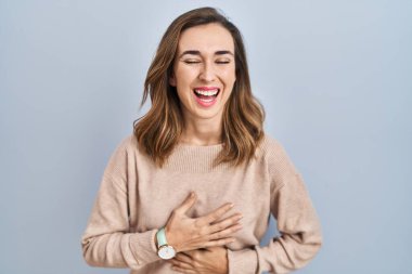 Young woman standing over isolated background smiling and laughing hard out loud because funny crazy joke with hands on body. 