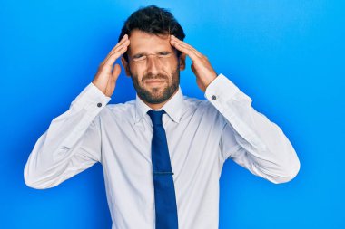 Sakallı, iş gömleği giyen ve eli kafasında kravat takan yakışıklı bir adam. Stres yüzünden başı ağrıyor. migren ağrısı. 