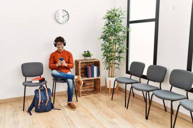 Genç İspanyol adam, bekleme odasında müzik dinlerken kendinden emin bir şekilde gülümsüyor.