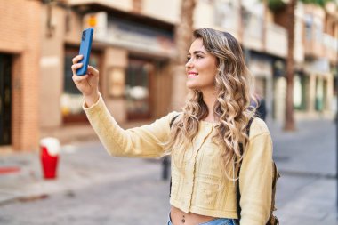 Genç bayan turist sokakta akıllı telefondan selfie çekiyor.