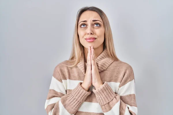 Young blonde woman wearing turtleneck sweater over isolated background begging and praying with hands together with hope expression on face very emotional and worried. begging.
