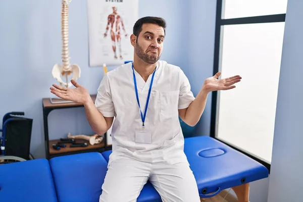Young Hispanic Man Beard Working Pain Recovery Clinic Clueless Confused — Stockfoto