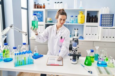 Laboratuvarda elinde şişe tutarken bilim adamı üniforması giyen genç bir kadın.