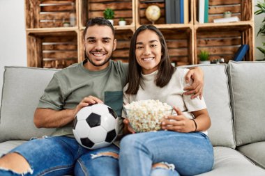Genç latin çift evde futbol maçı izleyip porpcorn yiyorlar..