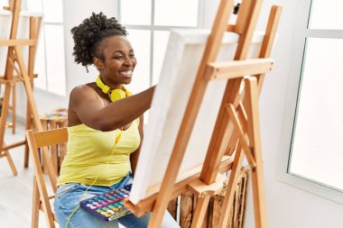 Genç Afrikalı Amerikalı kadın sanat stüdyosunda kulaklık kullanıyor..