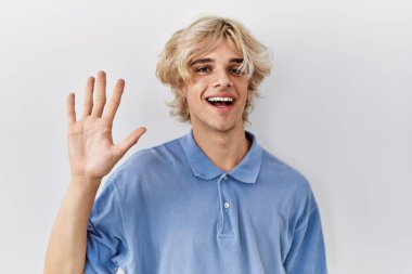 Genç modern adam izole edilmiş arka planda duruyor ve gülümserken beş numarayı işaret ediyor. Kendinden emin ve mutlu.. 