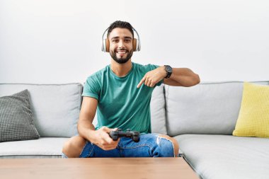 Yakışıklı, kulaklık takan, video oyunu oynayan, elinde kumandayla gülümseyen mutlu ve gururlu birini işaret eden bir İspanyol. 