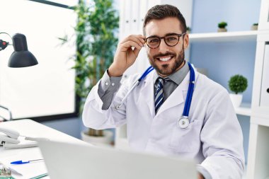 Klinikte çalışan dizüstü bilgisayar kullanan doktor üniforması giyen genç bir İspanyol.