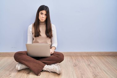 Bilgisayarla çalışan esmer bir kadın yerde depresif ve endişeli bir şekilde oturuyor. Kızgın ve korkmuş bir şekilde ağlıyor. hüzünlü ifade. 