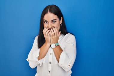 Mavi arka planda dikilen genç İspanyol kadın gülüyor ve utanıyor kıkır kıkır kıkır kıkır gülüyor elleri, dedikoduları ve skandalları anlatıyor 