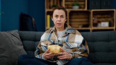 Orta yaşlı İspanyol kadın evde film izlerken patates kızartması yiyor.