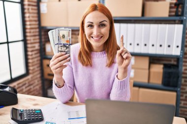 Küçük işletme şirketinde çalışan genç bir kadın elinde parayla bir fikir veya soruyla gülümsüyor ve mutlu bir yüzle işaret ediyor. 