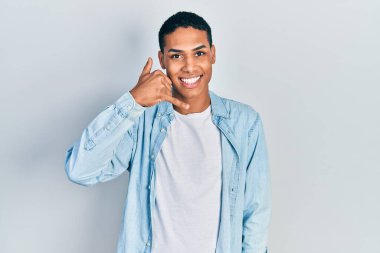 Genç Afro-Amerikan adam günlük kıyafetler giyip gülümsüyor telefonla el ve parmaklarıyla jest yapıyor telefonda konuşuyor gibi. iletişim kavramları. 