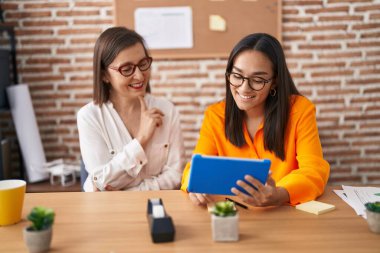 Two women business workers using touchpad working at office