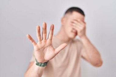 İzole edilmiş arka planda duran genç adam elleriyle gözlerini kapatıyor ve üzgün ve korku ifadeleriyle jest yapıyor. utangaç ve olumsuz kavram. 