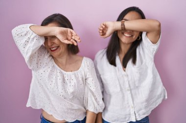 Hispanic mother and daughter together covering eyes with arm smiling cheerful and funny. blind concept. 