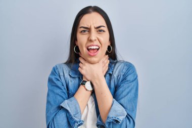 Hispanic woman standing over blue background shouting suffocate because painful strangle. health problem. asphyxiate and suicide concept. 