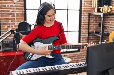 Young woman artist playing electrical guitar at music studio
