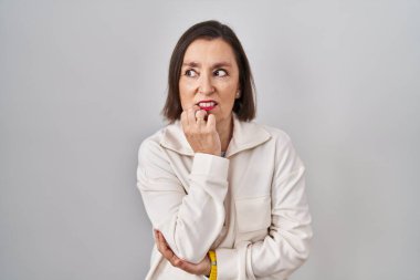 Middle age hispanic woman standing over isolated background looking stressed and nervous with hands on mouth biting nails. anxiety problem. 